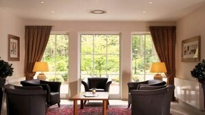 A spacious room with a large window, two armchairs, a coffee table, and two lamps. - Waldhotel Nachtigall (Paderborn)