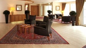 A spacious lobby with a large seating area, a reception desk, and a large window with curtains. - Waldhotel Nachtigall (Paderborn)