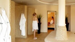 A spa area with a circular stone feature, a mirror, and a person in a robe. - Waldhotel Nachtigall (Paderborn)