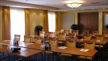 A conference room with multiple tables and chairs, equipped with a projector and a large window with curtains.