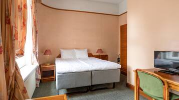 Una camera d'albergo con un letto, una scrivania, una sedia, un televisore e una finestra con tende.