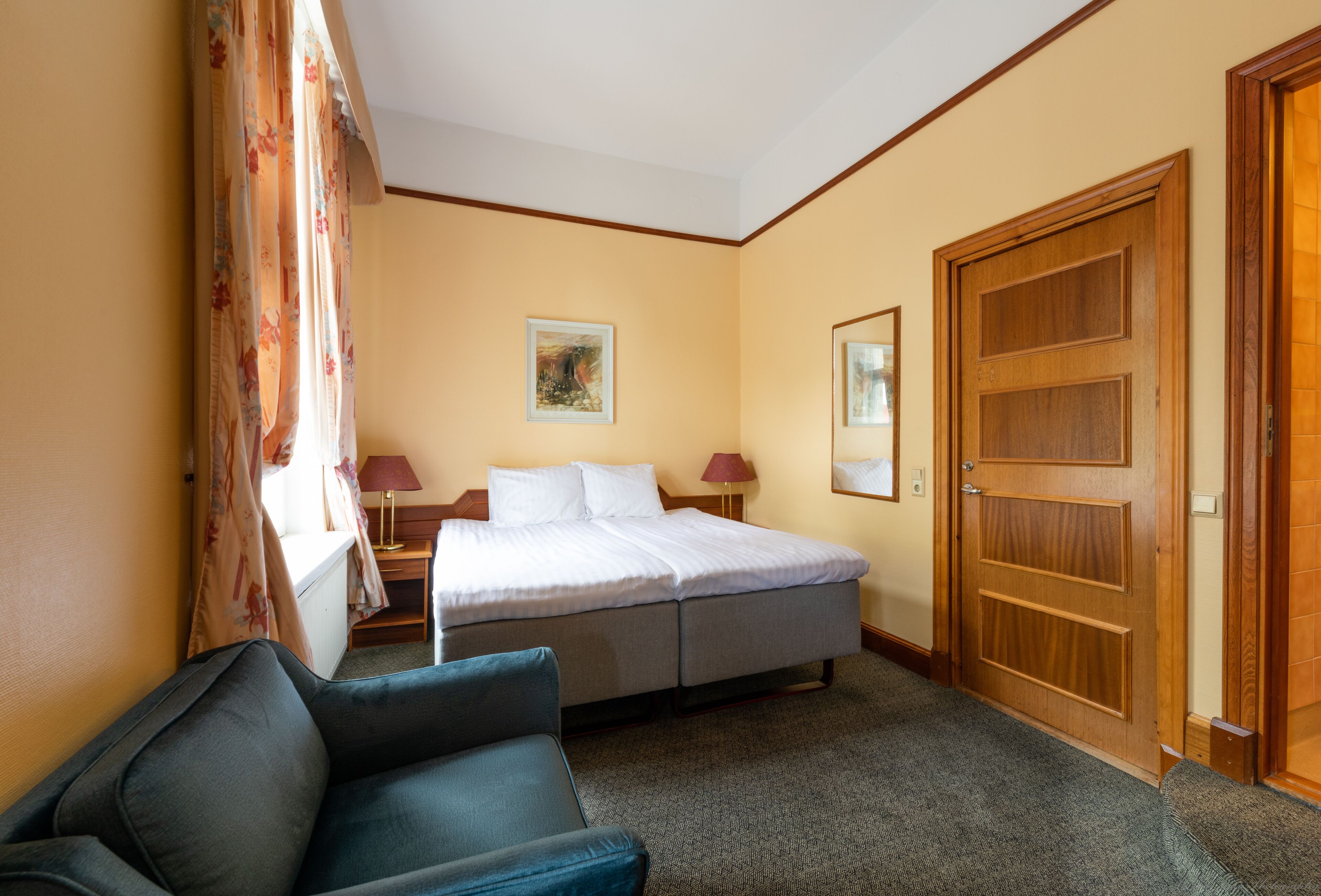 A hotel room with a bed, a desk, a chair, and a door.