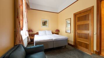 A hotel room with a bed, a desk, a chair, and a door.