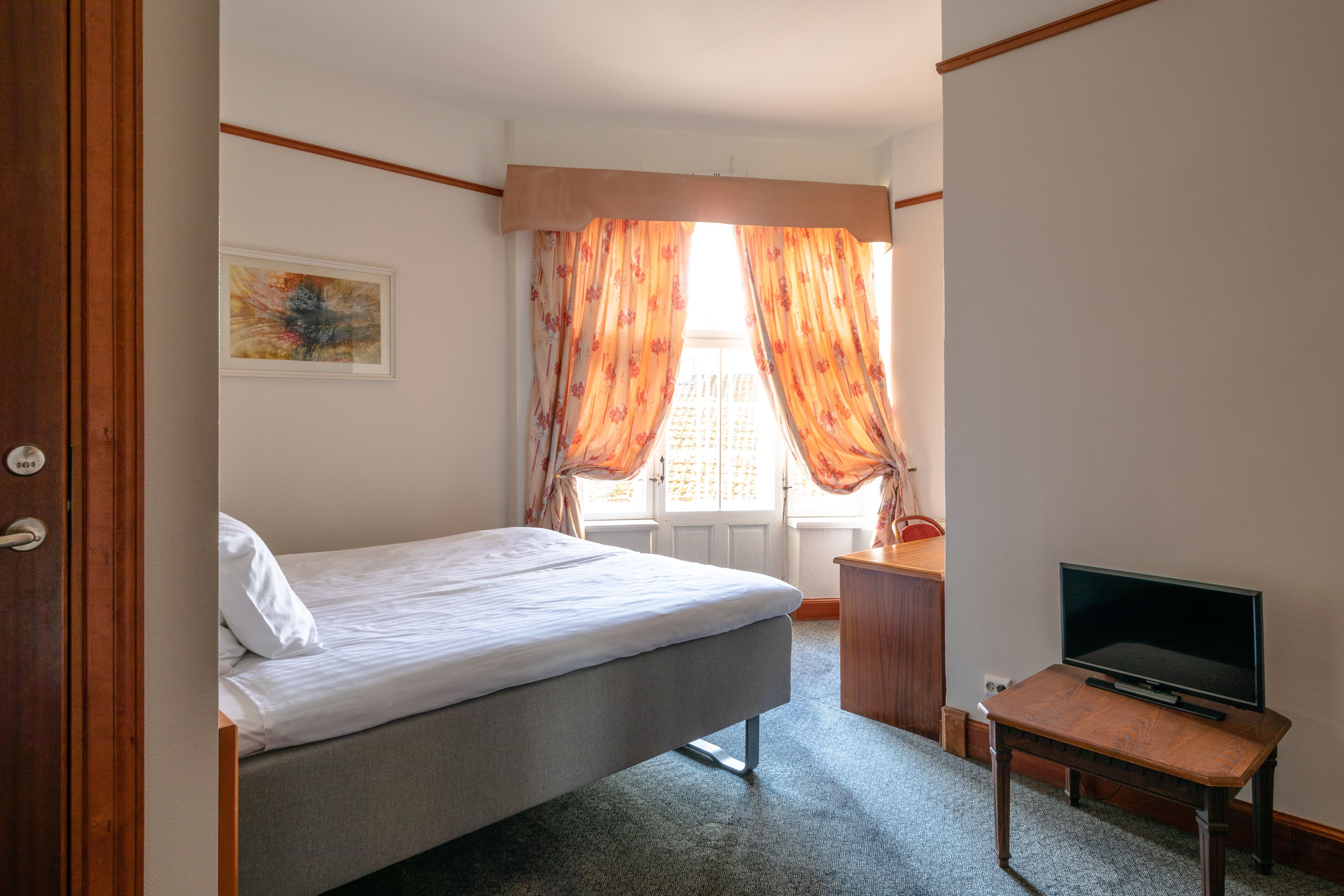 Una camera d'albergo con un letto, una televisione su un tavolino di legno e una finestra con tende.