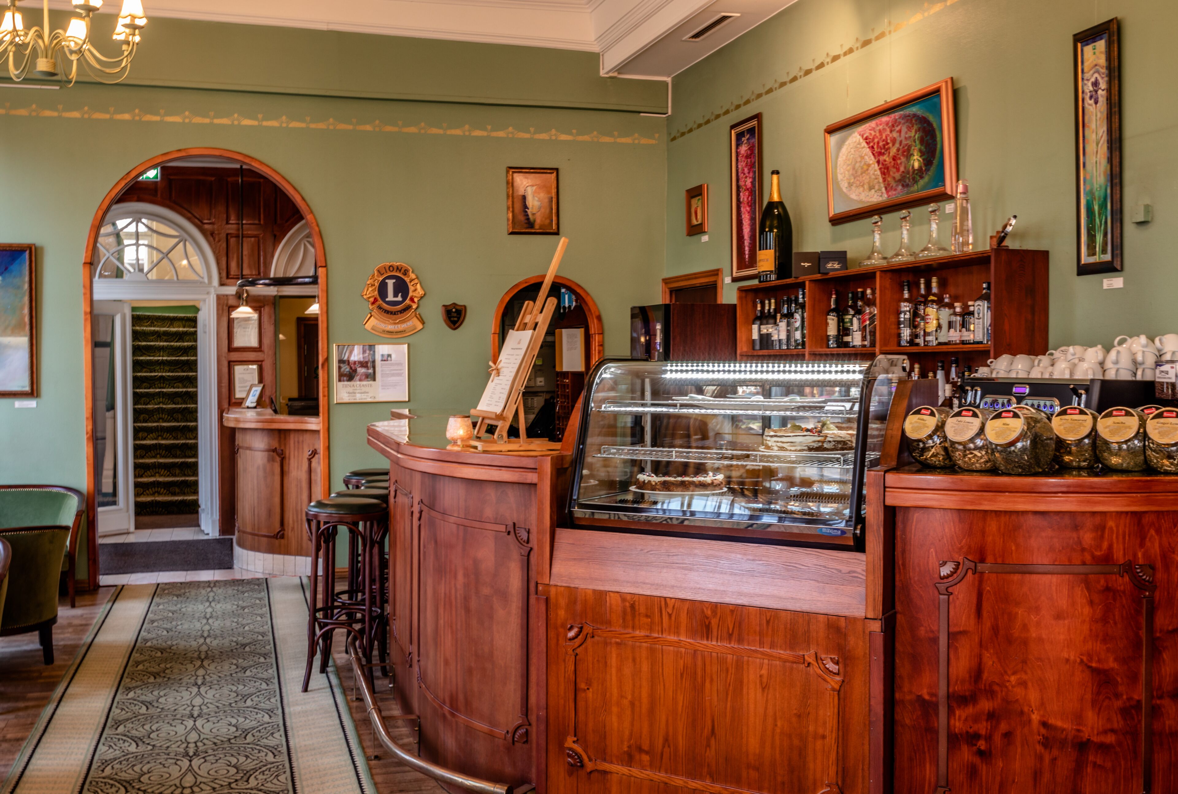 Een bar met houten kasten, een vitrine met gebak, en een groene wand met ingelijste foto's.