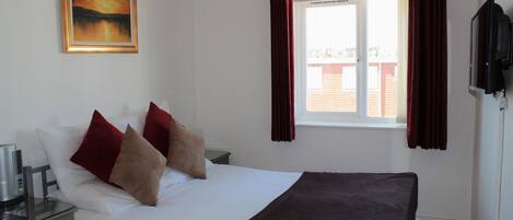 A hotel room with a bed, a nightstand, a TV, a window with curtains, and a painting on the wall.