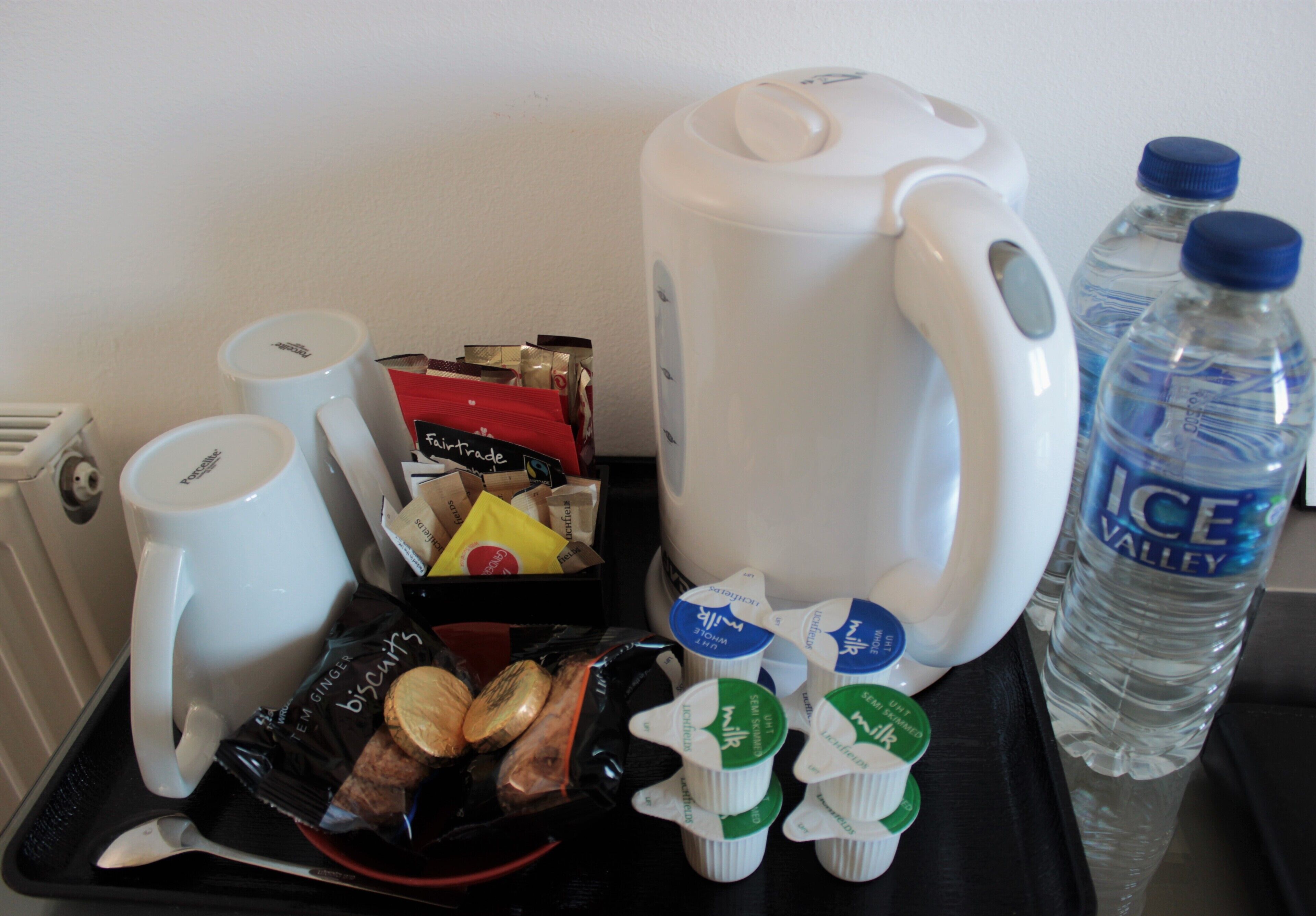 Una bandeja con cafetera, tazas, galletas, cartones de leche y una botella de agua.