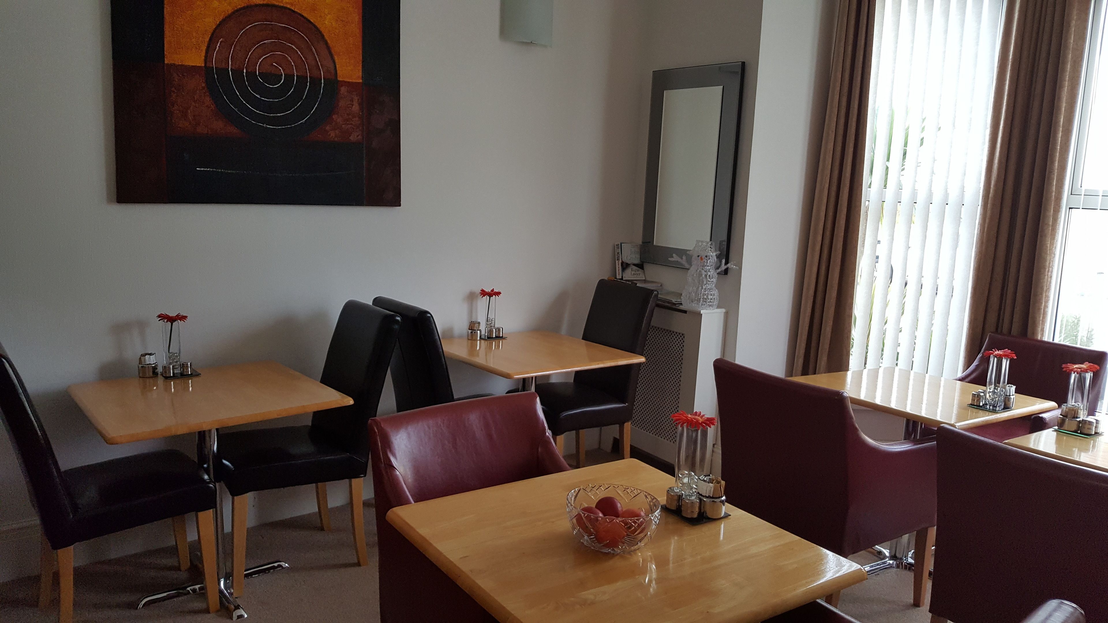 Habitación de hotel con zona de comedor que incluye dos mesas y cuatro sillas, un cuadro en la pared, un espejo y una ventana con cortinas.