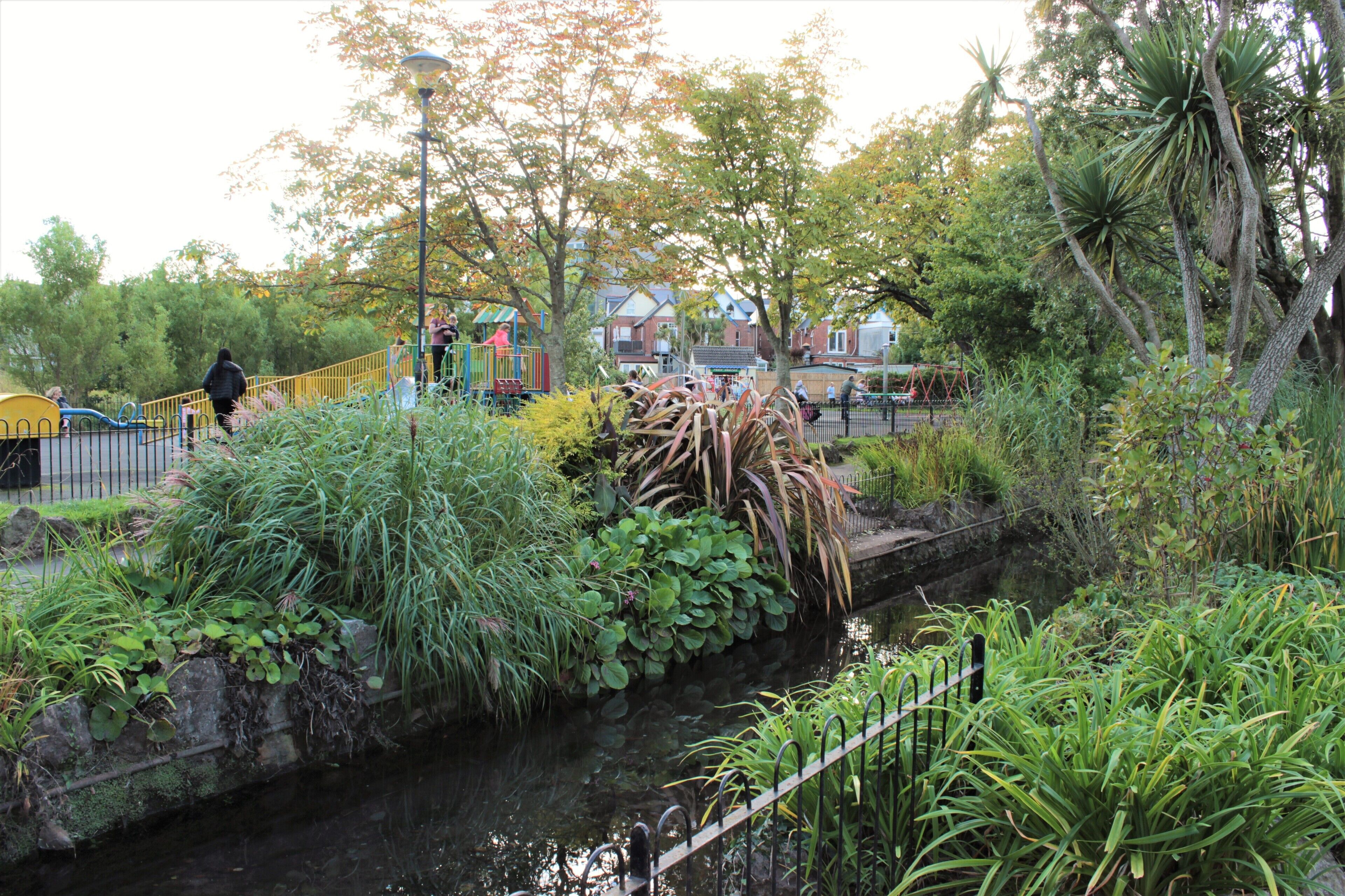 A park with a playground, a small water channel, and various plants.