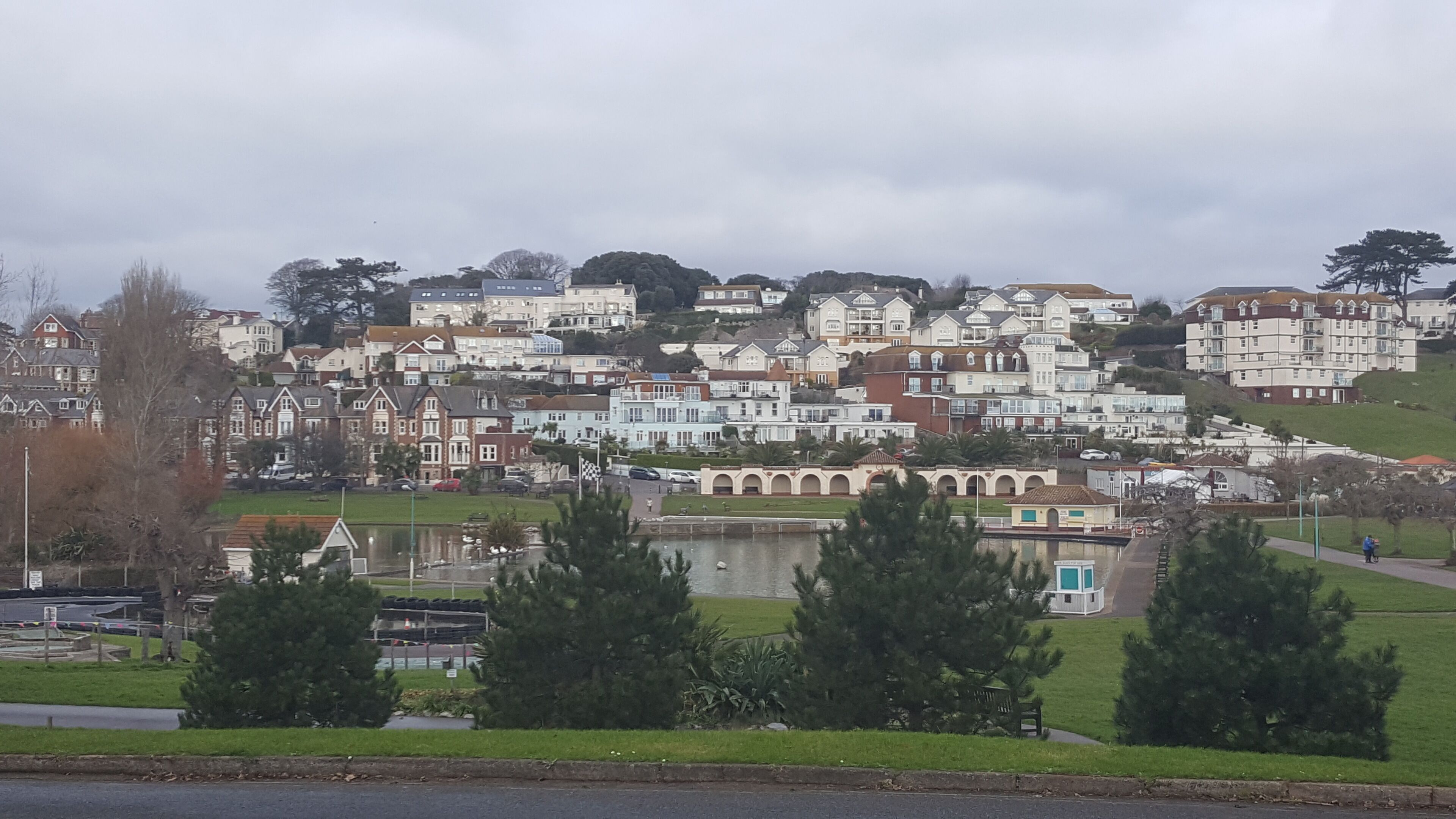 Zona residencial costera con casas en una ladera, un lago pequeño y un sendero peatonal.