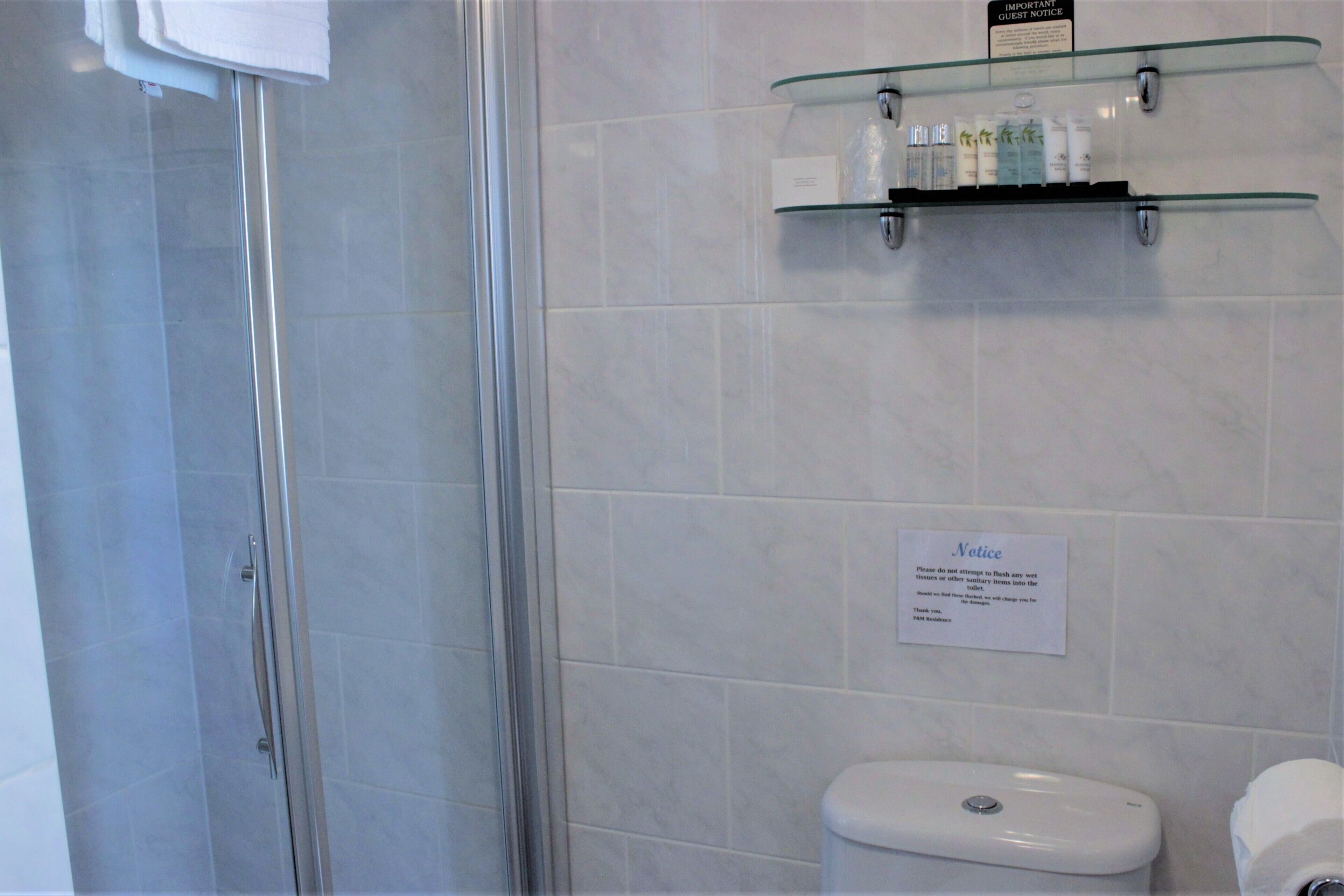 Un baño con cabina de ducha de vidrio, inodoro y estante con artículos de aseo.