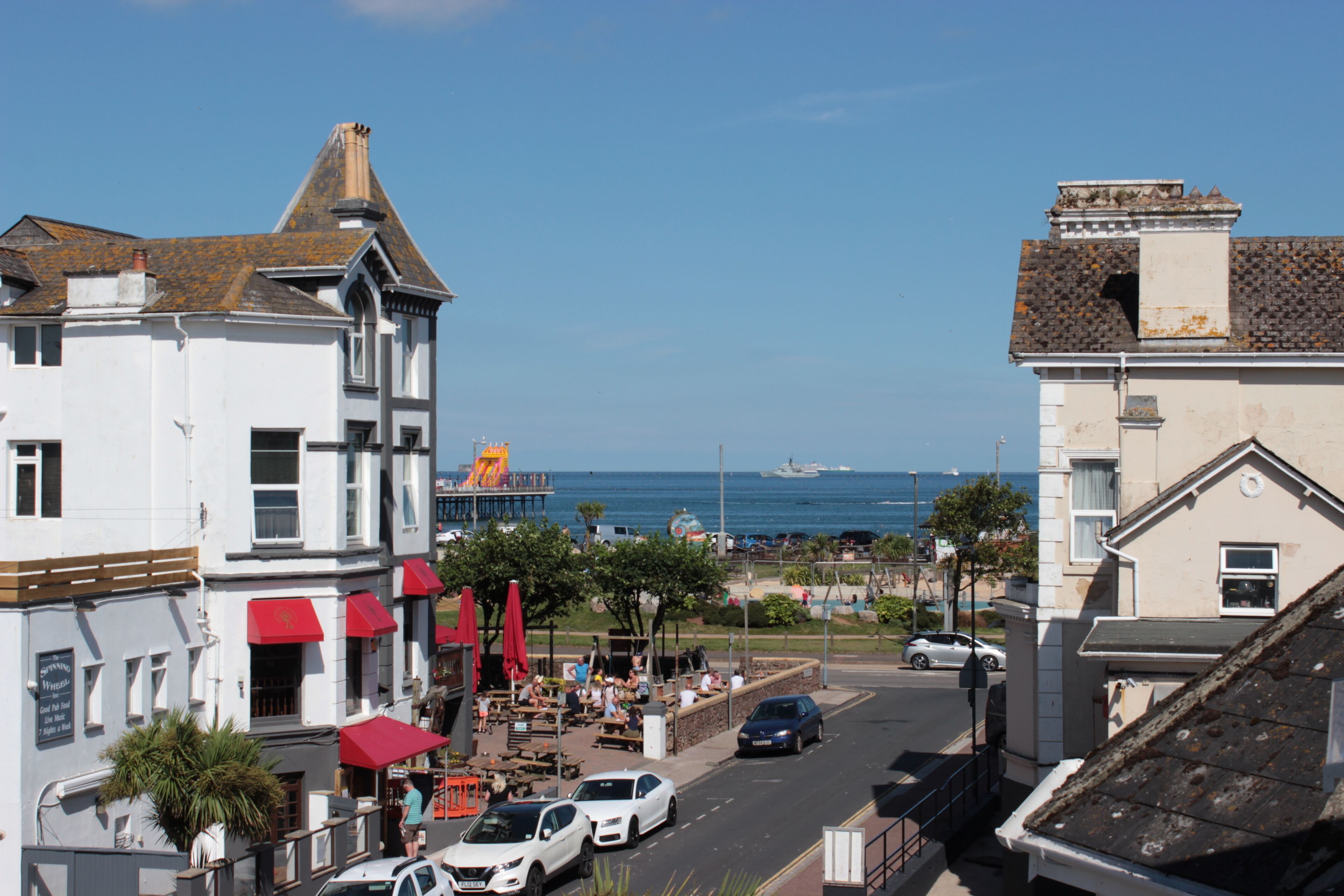 Eine Küstenstadt mit einem weißen Gebäude, das rote Markisen hat, einem Restaurant mit Außenbereich und Blick auf das Meer.