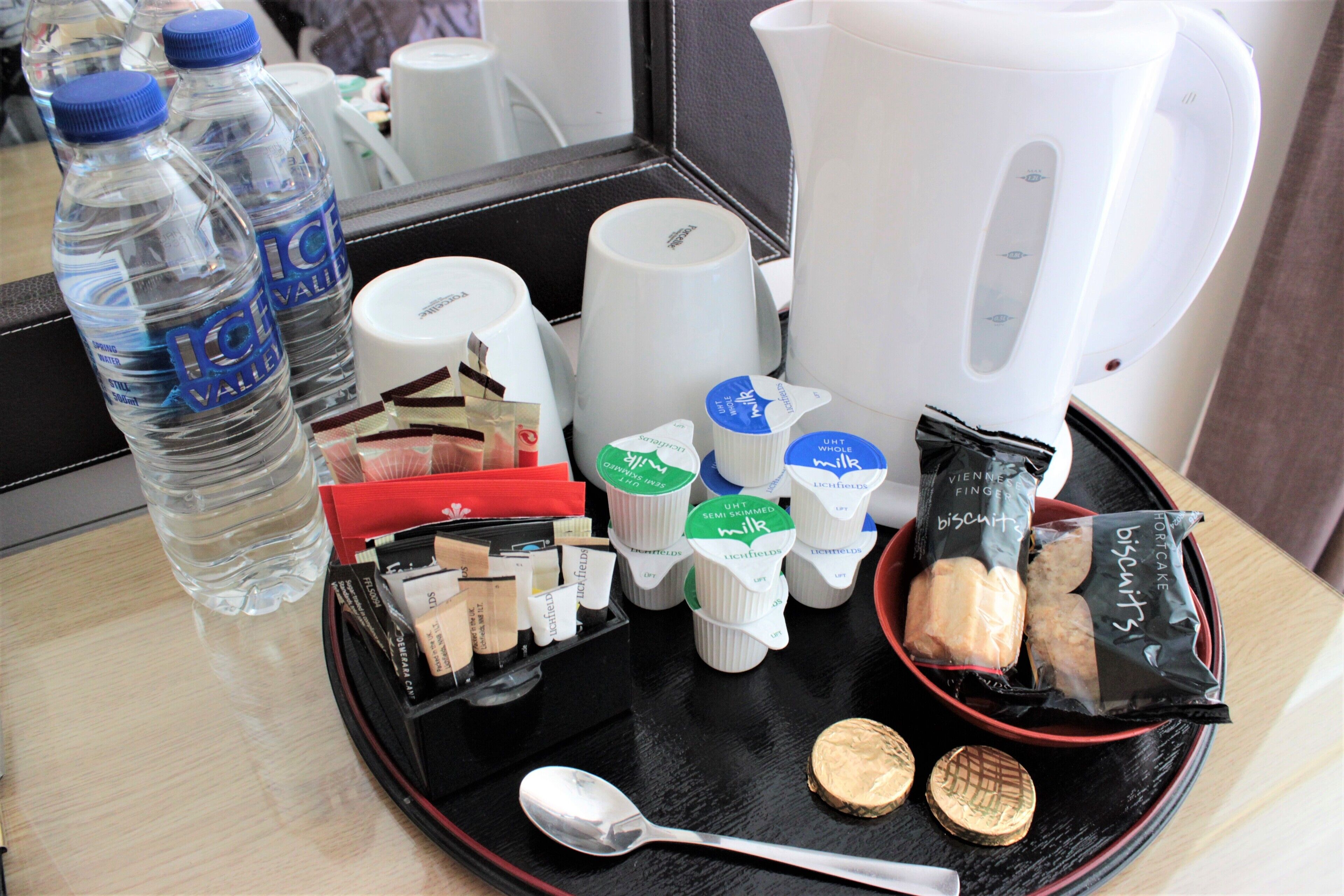 Una bandeja con botellas de agua, una cafetera, diversos alimentos y una cuchara.