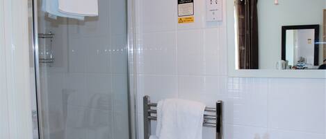 A bathroom with a glass shower enclosure, a towel rack with a white towel, a sink with a soap dispenser, and a mirror with a brown curtain.
