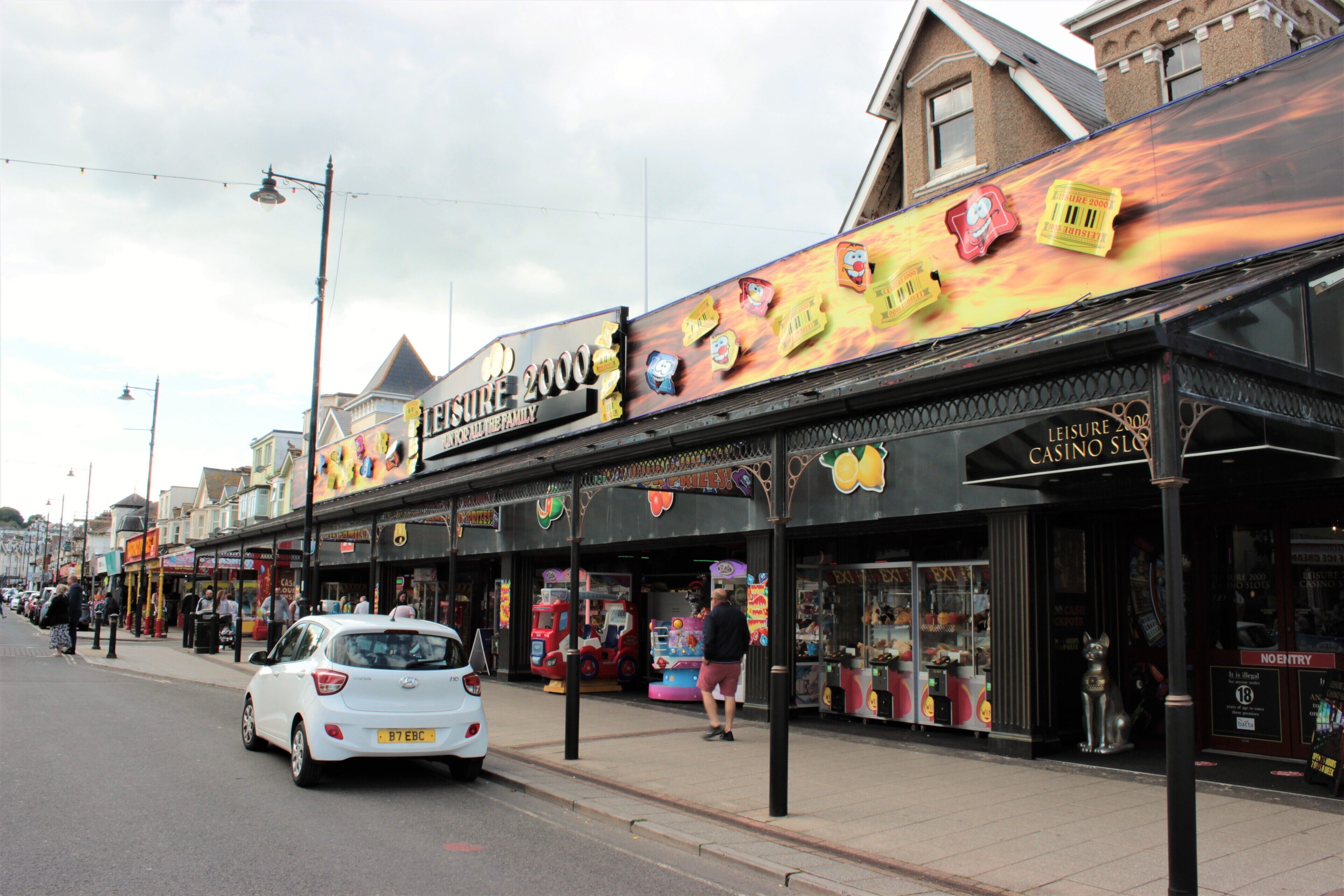 A row of shops with a prominent casino sign, a white car parked on the street, and a pedestrian walkway.