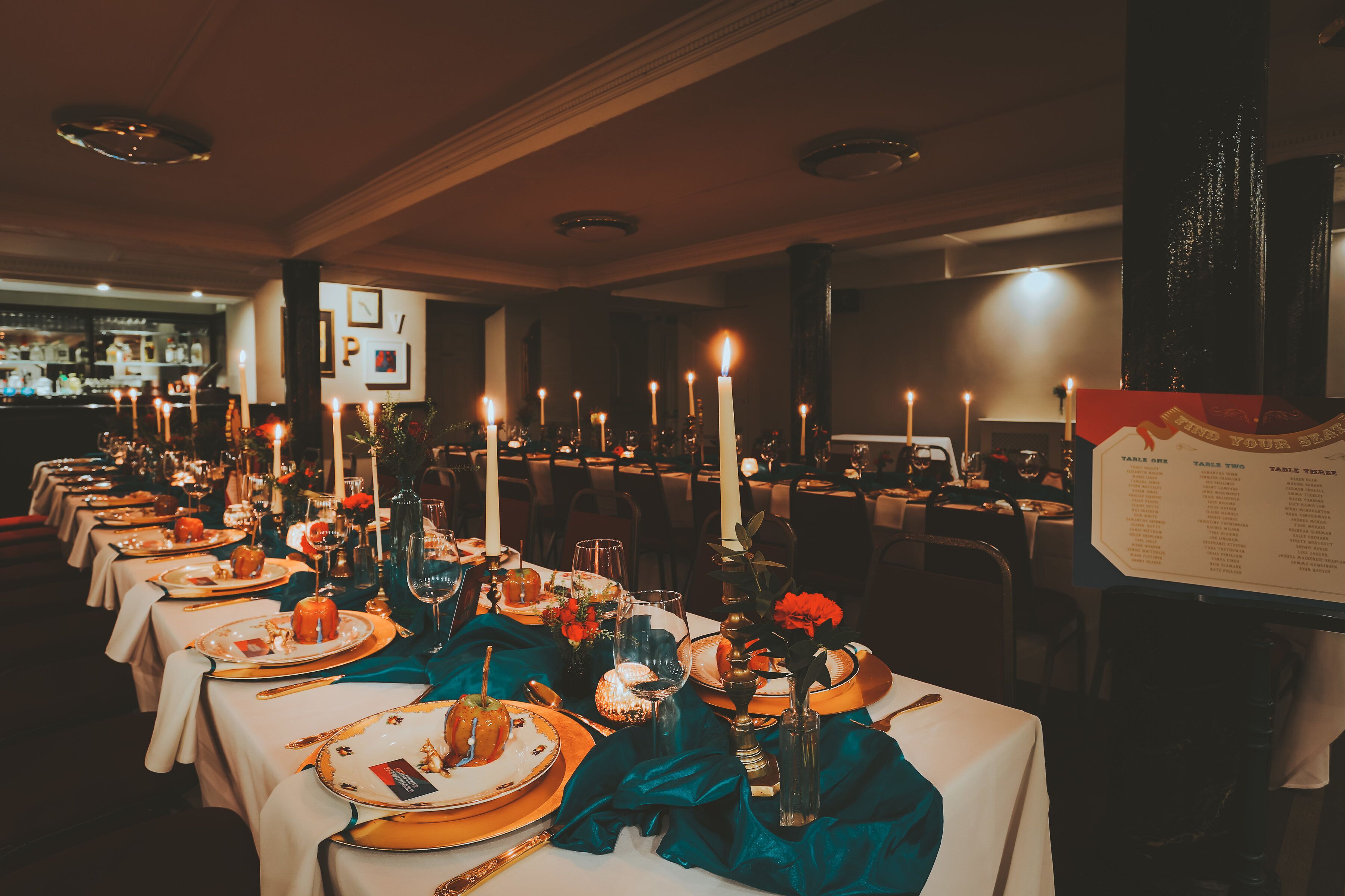 A long dining table set with multiple candles, plates, and glasses, indicating a formal dining arrangement.