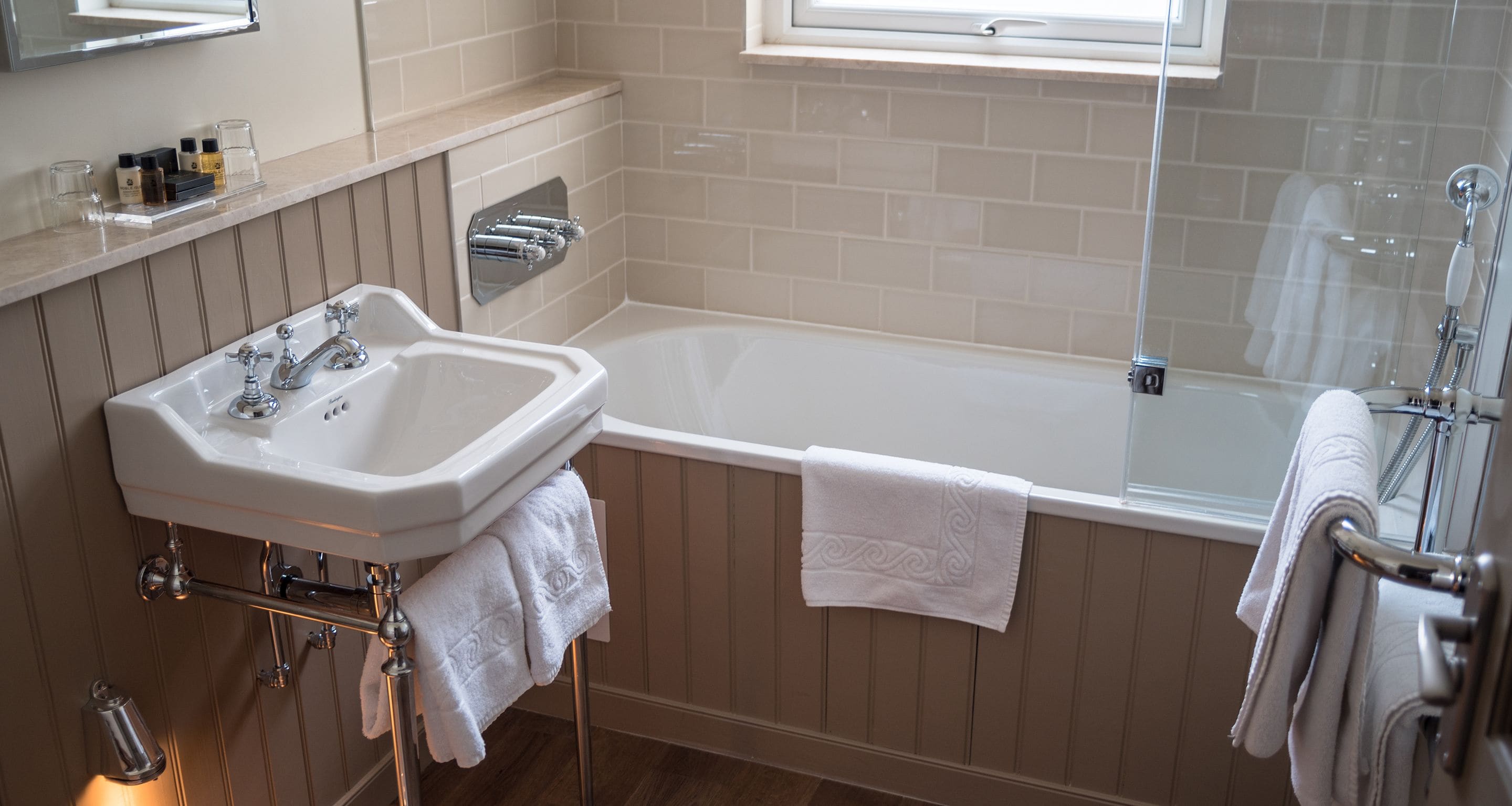 Une salle de bain avec un lavabo, une baignoire et une douche. Des serviettes sont accrochées au mur et il y a une fenêtre au-dessus de la baignoire.