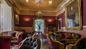 A luxurious room with a large leather armchair, multiple sofas, a chandelier, and a large portrait on the wall. - Penventon Park Hotel (Redruth)