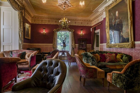 A luxurious room with a large leather armchair, multiple sofas, a chandelier, and a large portrait on the wall.