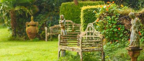 A garden with a bench, statues, and a well-maintained hedge.