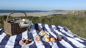 A picnic setup with a wicker basket, sandwiches, pastries, and drinks on a striped blanket by the beach. - Penventon Park Hotel (Redruth)