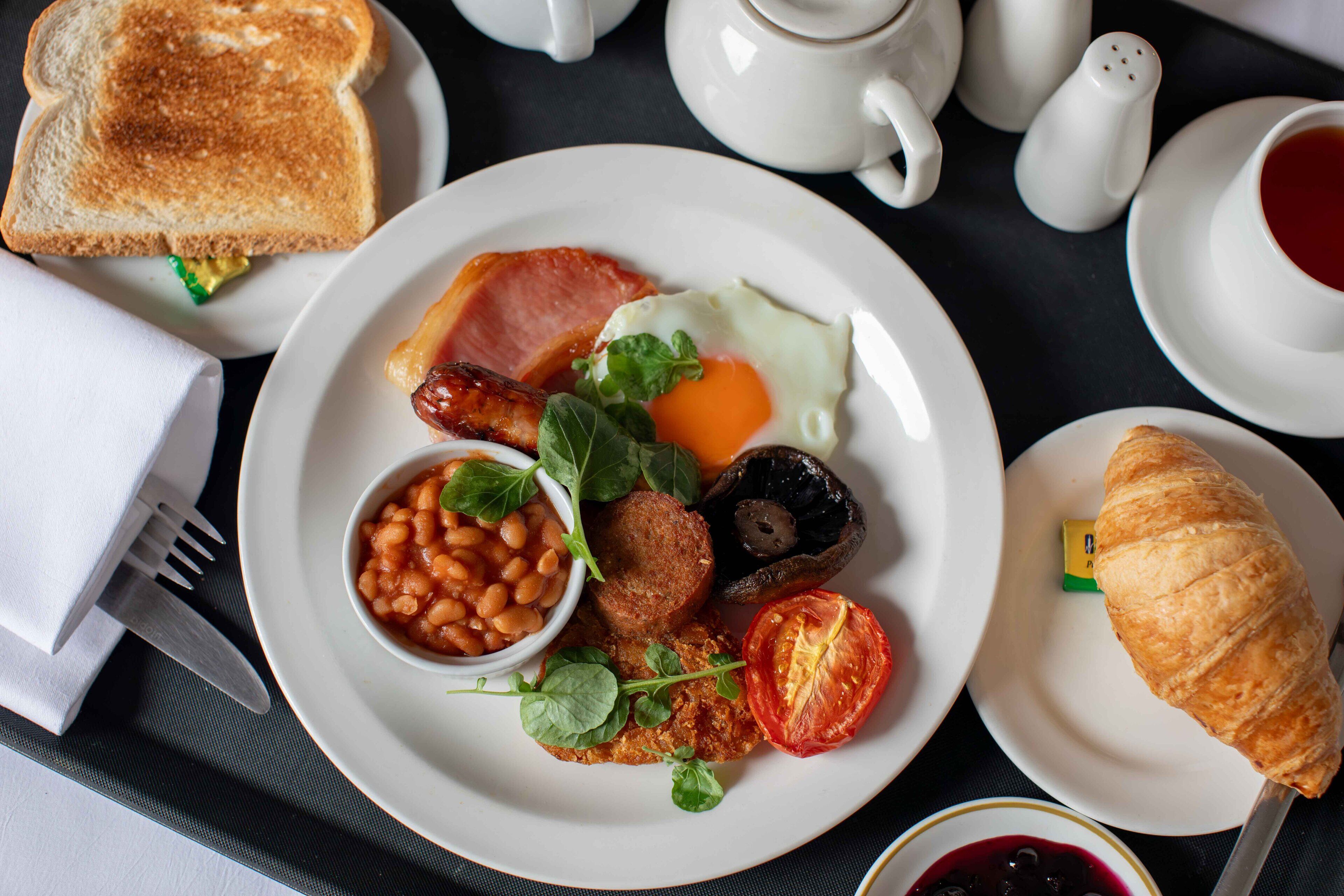 A breakfast plate with toast, eggs, bacon, beans, mushrooms, and a tomato.