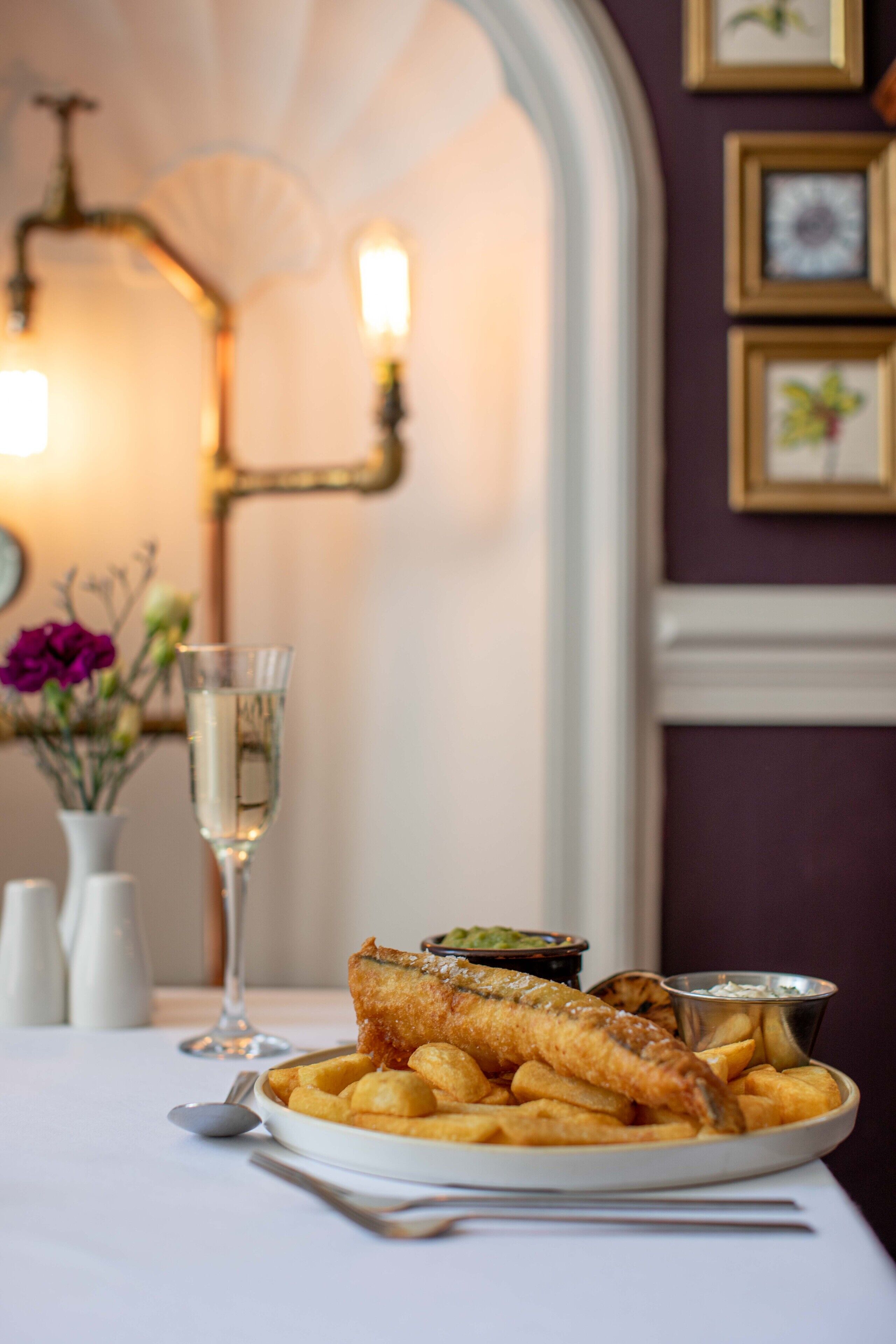 A plate of fish and chips with a glass of water on a table.