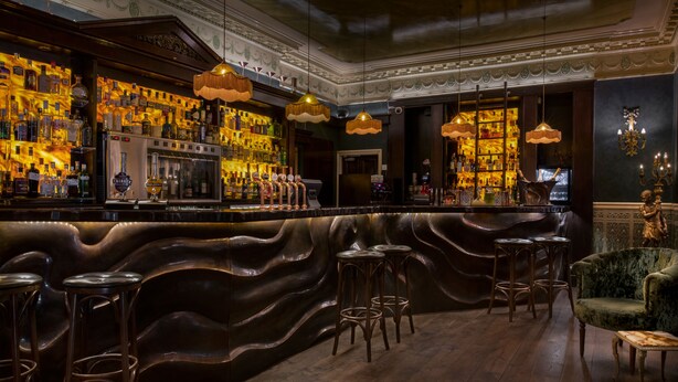 A bar area with a wavy counter, multiple stools, and a variety of bottles and glasses. - Penventon Park Hotel (Redruth)