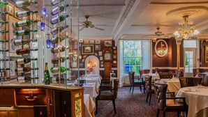 A dining area with tables set for service, a wall of wine bottles, and a chandelier. - Penventon Park Hotel (Redruth)