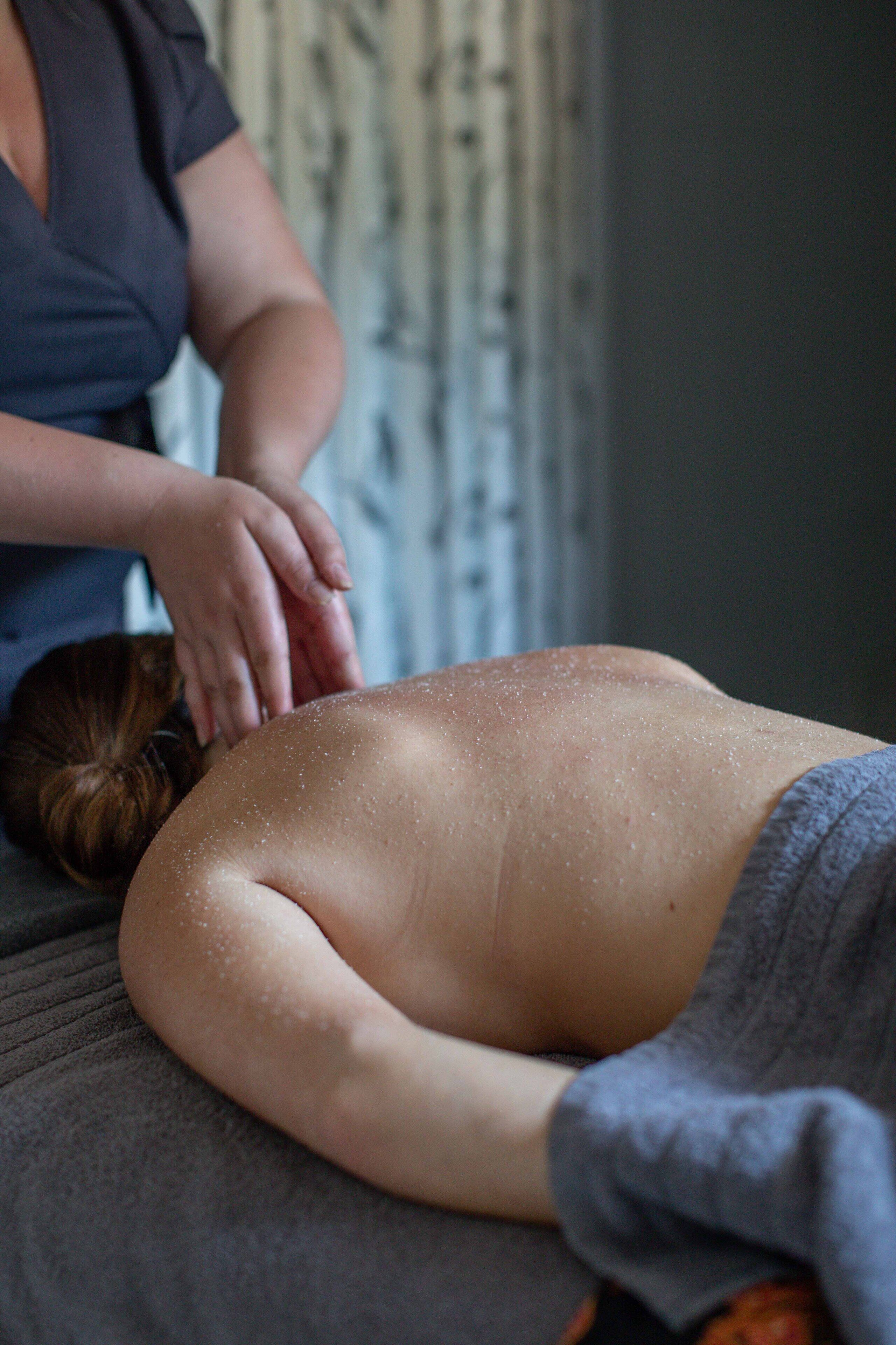 A person lying face down on a massage table receiving a back massage.