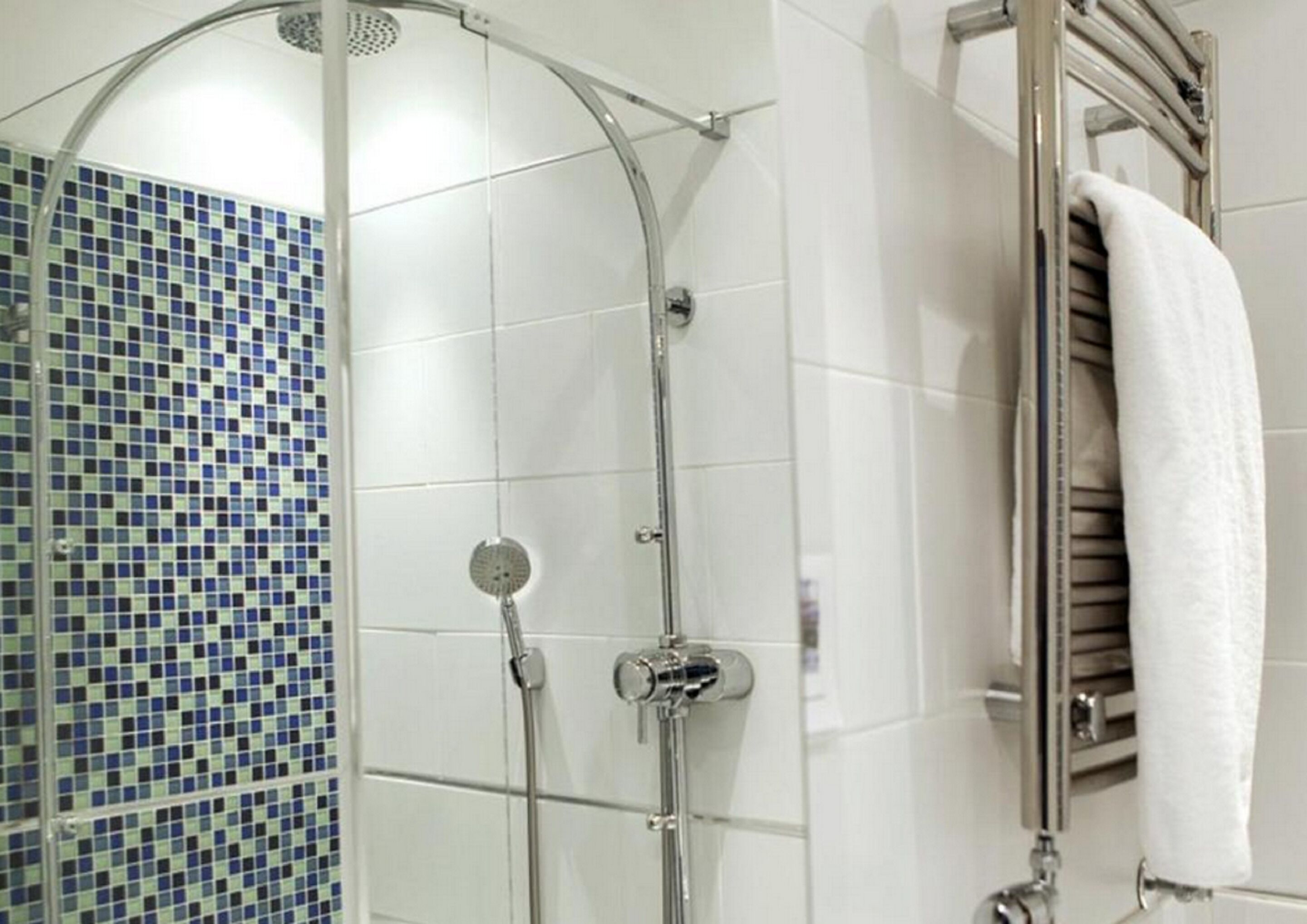 Um chuveiro com porta de vidro curva, parede revestida de azulejos brancos e porta-toalhas com uma toalha branca.