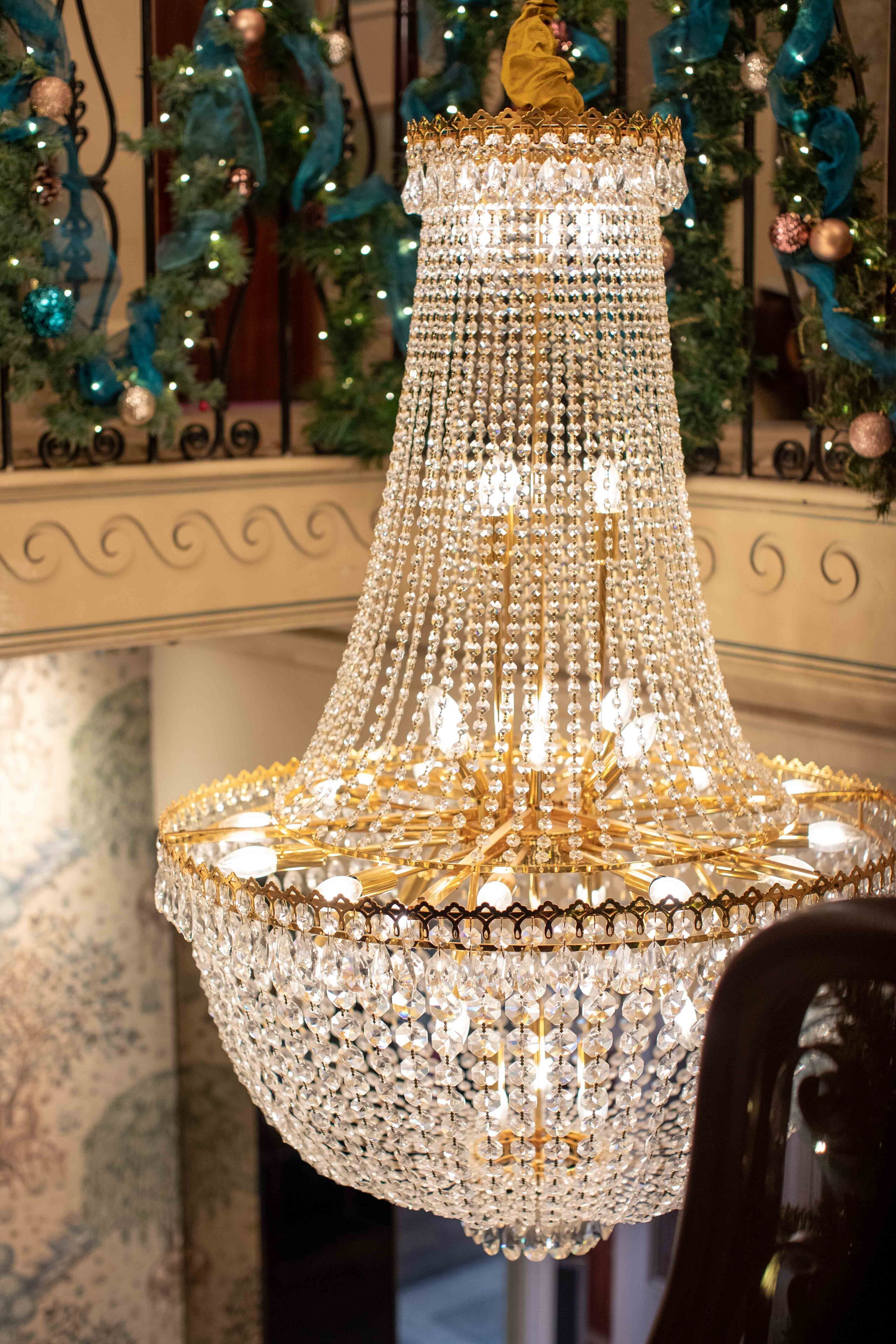 A chandelier with multiple tiers of crystals and gold accents, set against a backdrop of a decorated interior space.