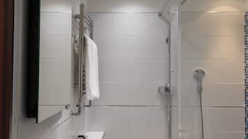 A modern bathroom with white tiles, a glass shower enclosure, a towel hanging on a rack, and a small sink with toiletries.