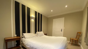 A bedroom with a large bed, a bedside table, a chair, a door, and a wall with vertical stripes.