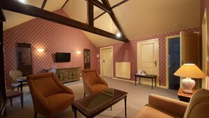 A cozy room with a high ceiling, a fireplace, a television, and a comfortable seating area with two armchairs and a sofa.