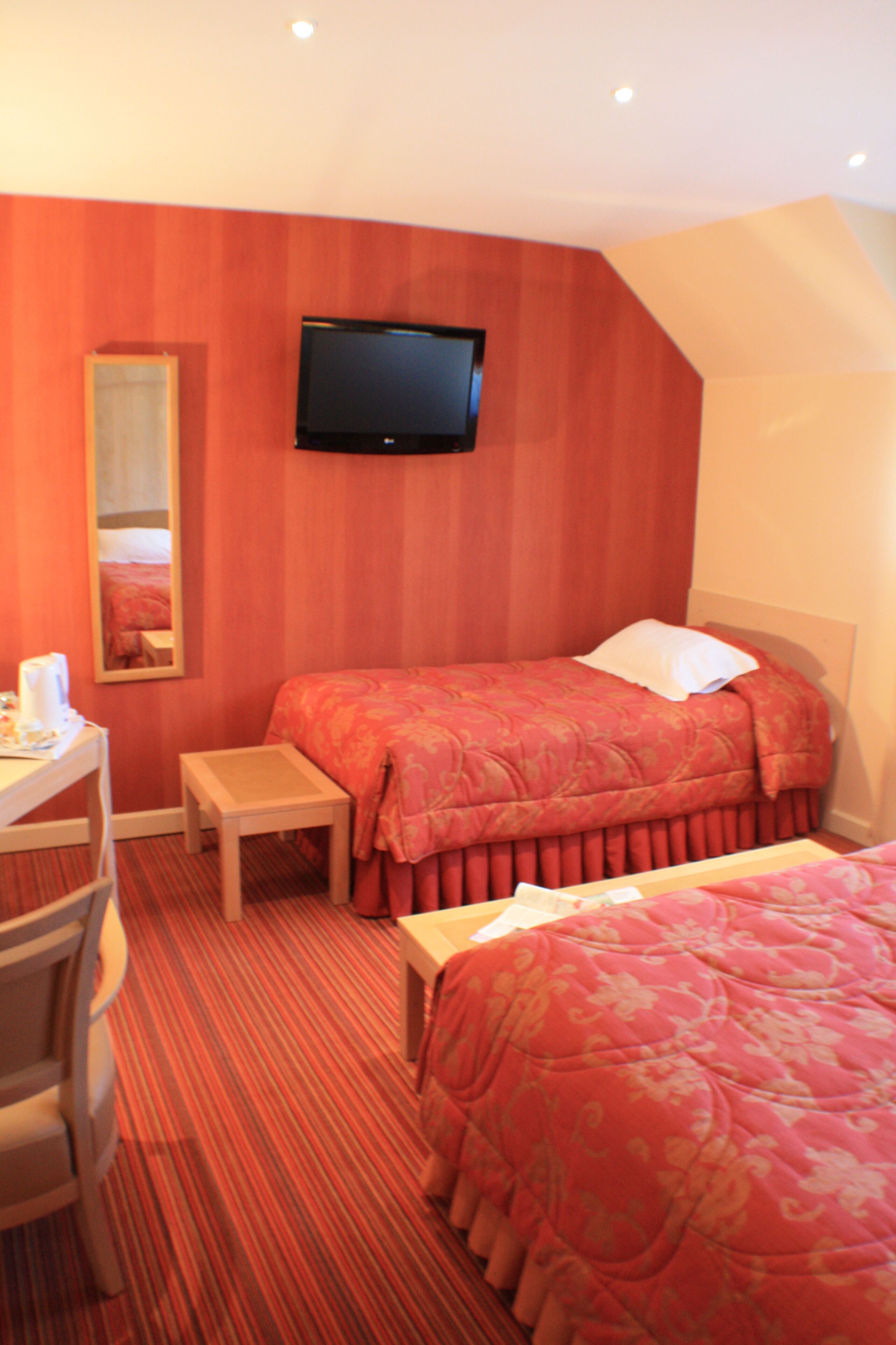Een hotelkamer met een bed, een bureau met stoel, een aan de muur bevestigde televisie en een kleine tafel.