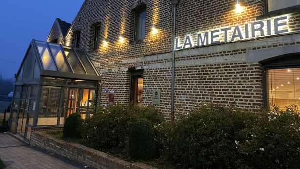 A building with a sign reading "LA METAIRIE" and a modern glass structure adjacent to it.