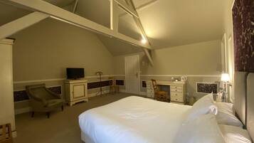 A bedroom with a large bed, a desk, a chair, a television, and a wardrobe.