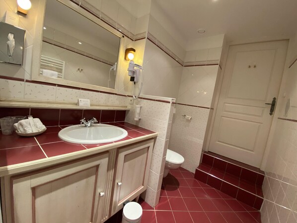 A bathroom with a white sink, a mirror, a toilet, and a door. - La Metairie (Gosnay)