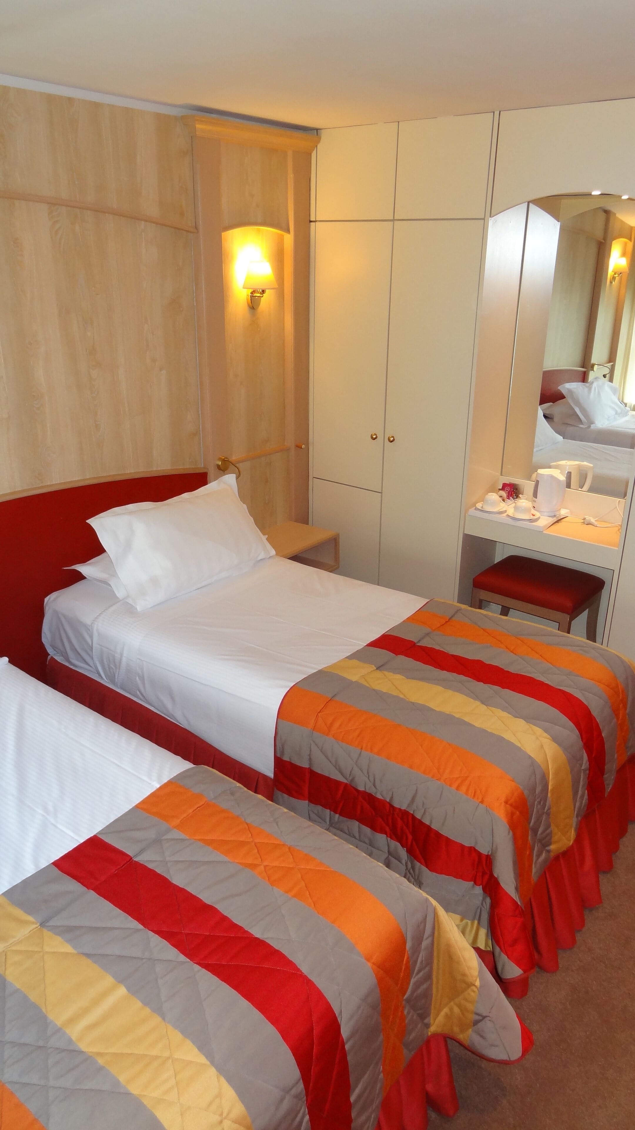 Une chambre d’hôtel avec deux lits, un bureau avec un miroir et une armoire.