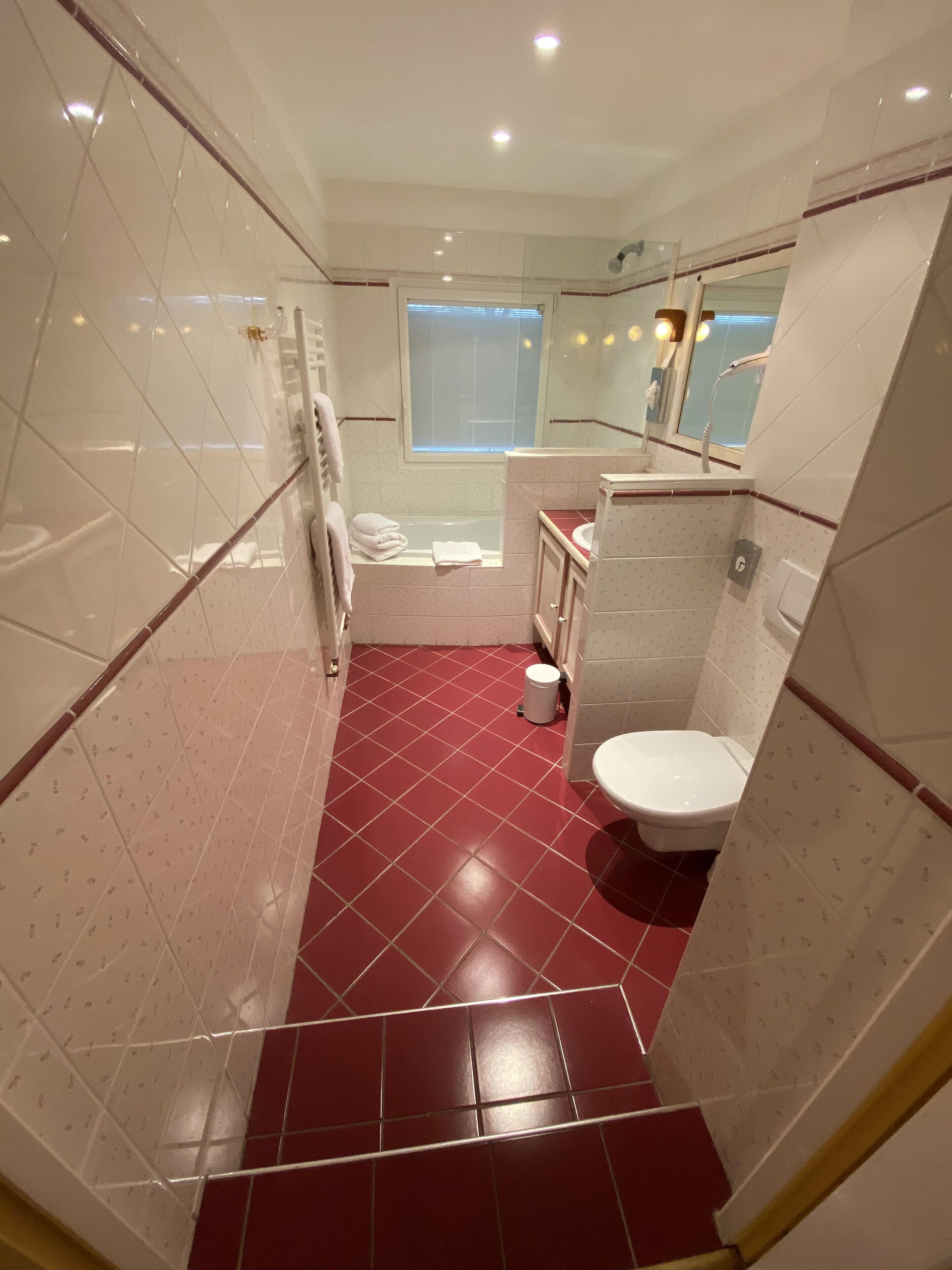 A bathroom with a red-tiled floor, a white toilet, a sink, and a bathtub.