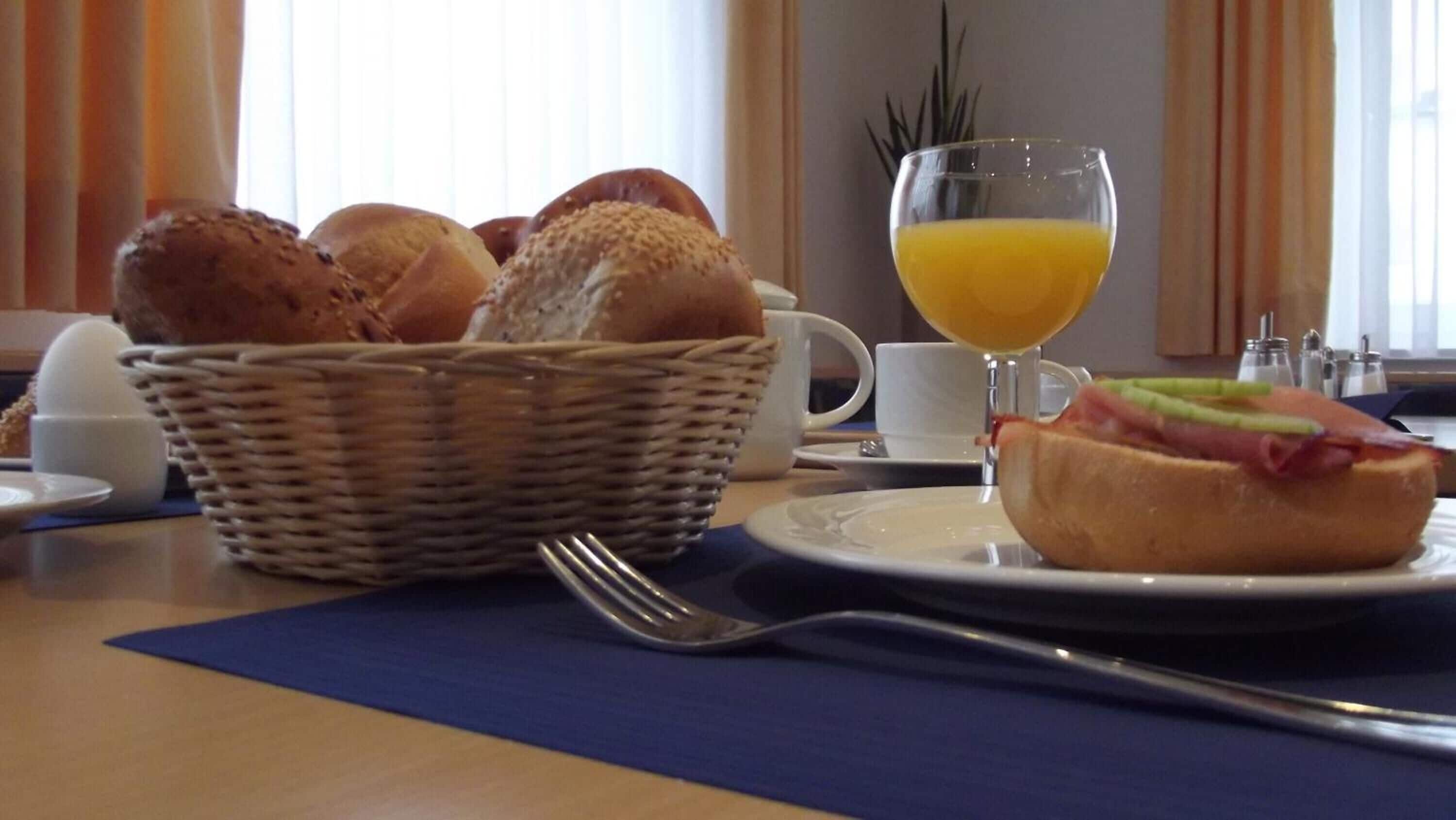 Ein Frühstückstisch mit Brot, einem Glas Orangensaft und einem Teller mit einem Sandwich.
