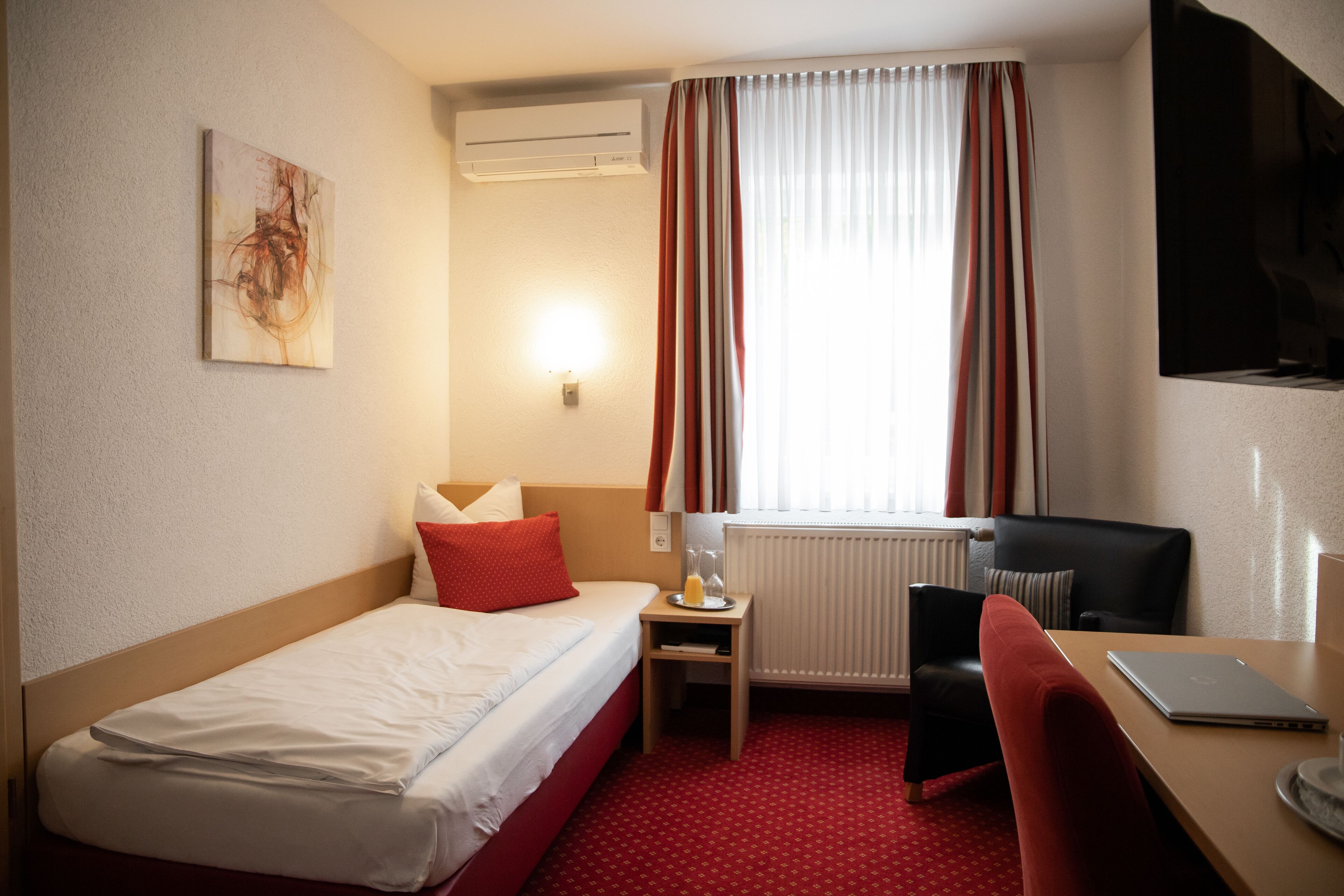 A hotel room with a bed, a desk, a chair, a TV, and a window with curtains.