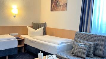 Ein Hotelzimmer mit zwei Betten, einem Sofa, einem kleinen Tisch mit Tasse und Gläsern sowie einem Bild an der Wand.