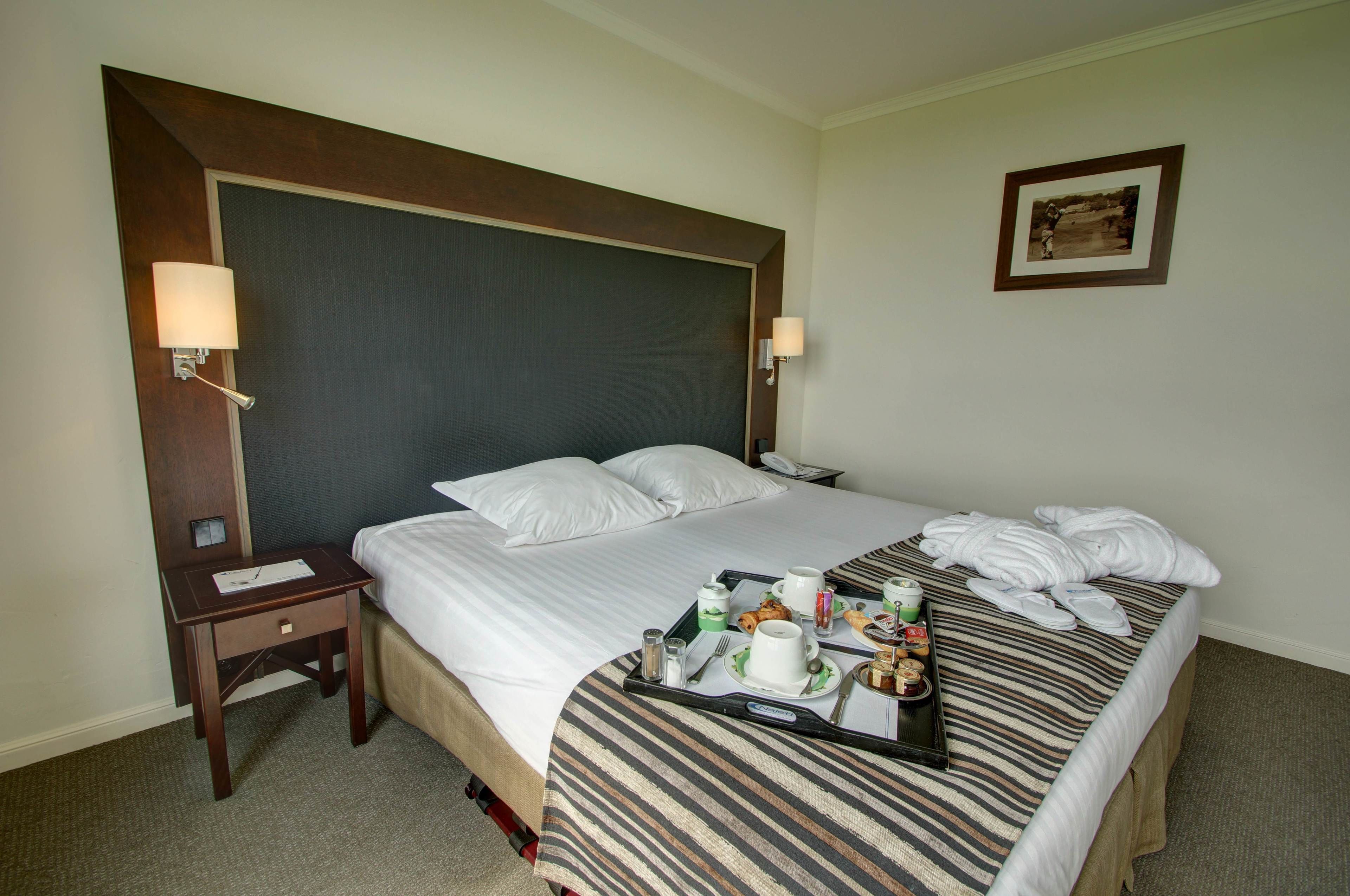 Een hotelkamer met een groot bed, een nachtkastje met een lamp en een dienblad met ontbijtartikelen.