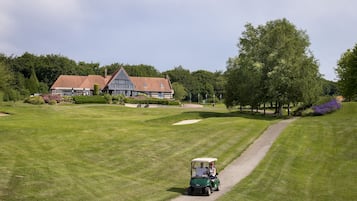 Een golfbaan met een clubhuis, een pad en een golfkar.
