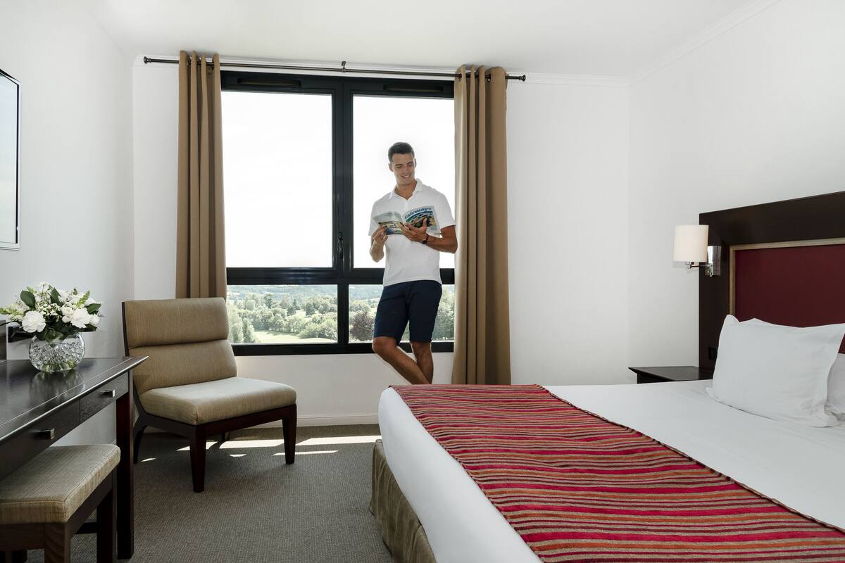 Habitación de hotel con una cama grande, un escritorio con silla, una ventana con cortinas y vistas al exterior.