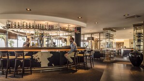 Zona de bar con varios taburetes, una barra con botellas y un jarrón grande.