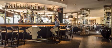 Zona de bar con varios taburetes, una barra con botellas y un jarrón grande.