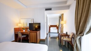 Une chambre d’hôtel avec un lit, un bureau avec un ordinateur, une télévision, une chaise, une lampe et un peignoir accroché au mur.